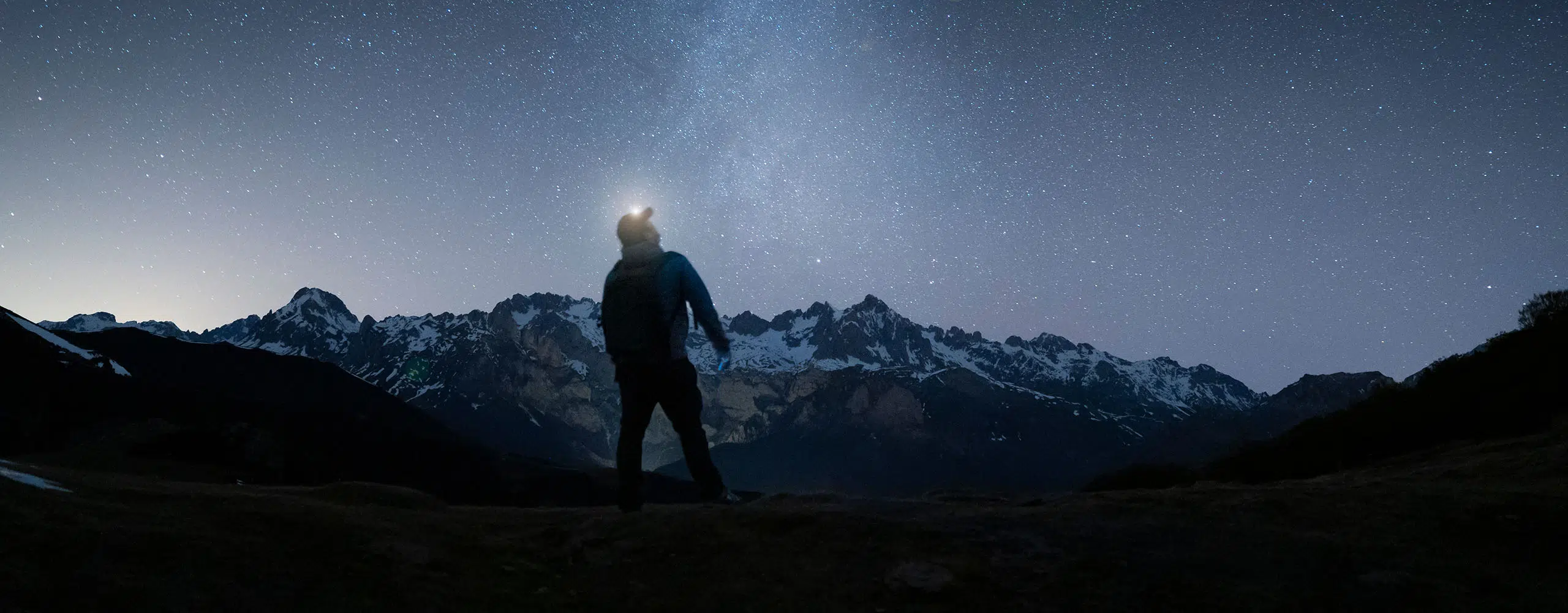 Person stargazing near snowy mountains at night