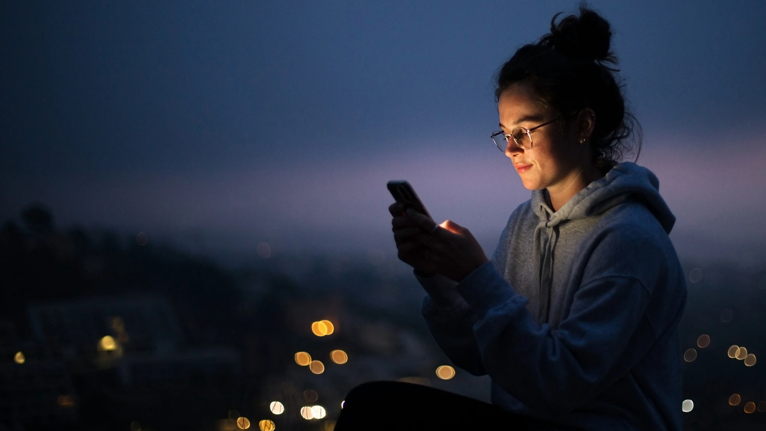 Person using smartphone at dusk with city lights