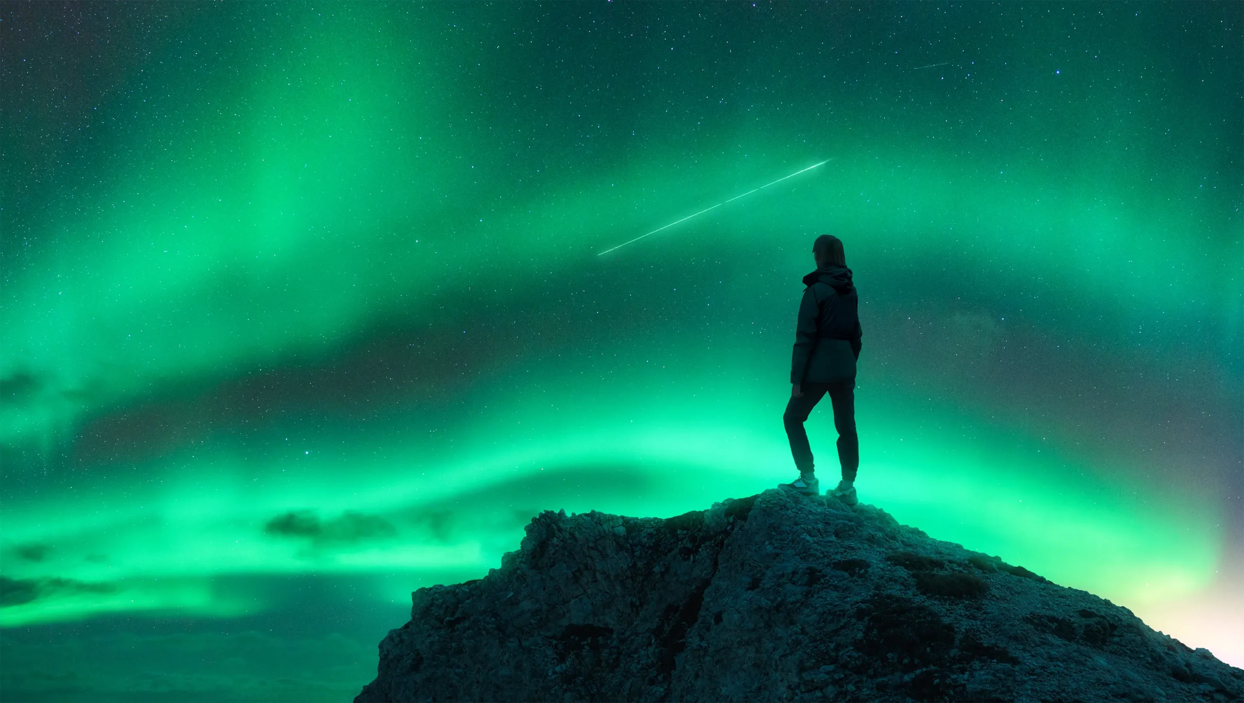 Person watching northern lights on rocky hill.