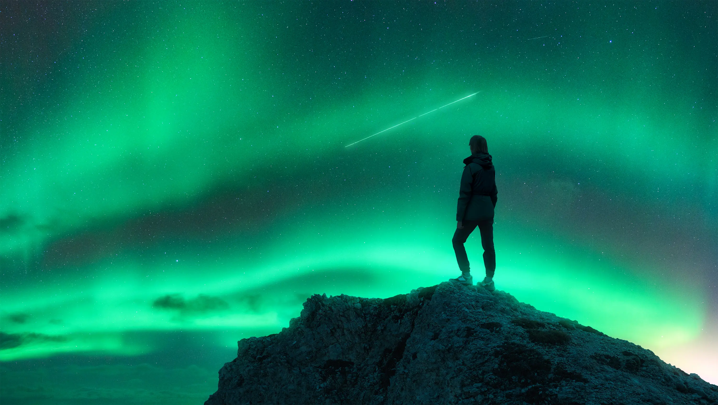 Person watching northern lights on rocky hill.